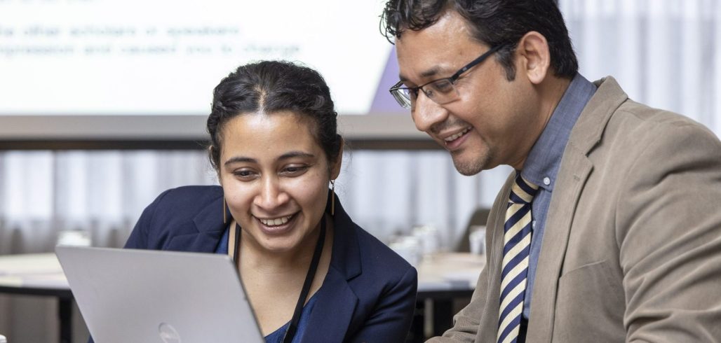 Two alumni collaborate on a laptop during an impact challenge
