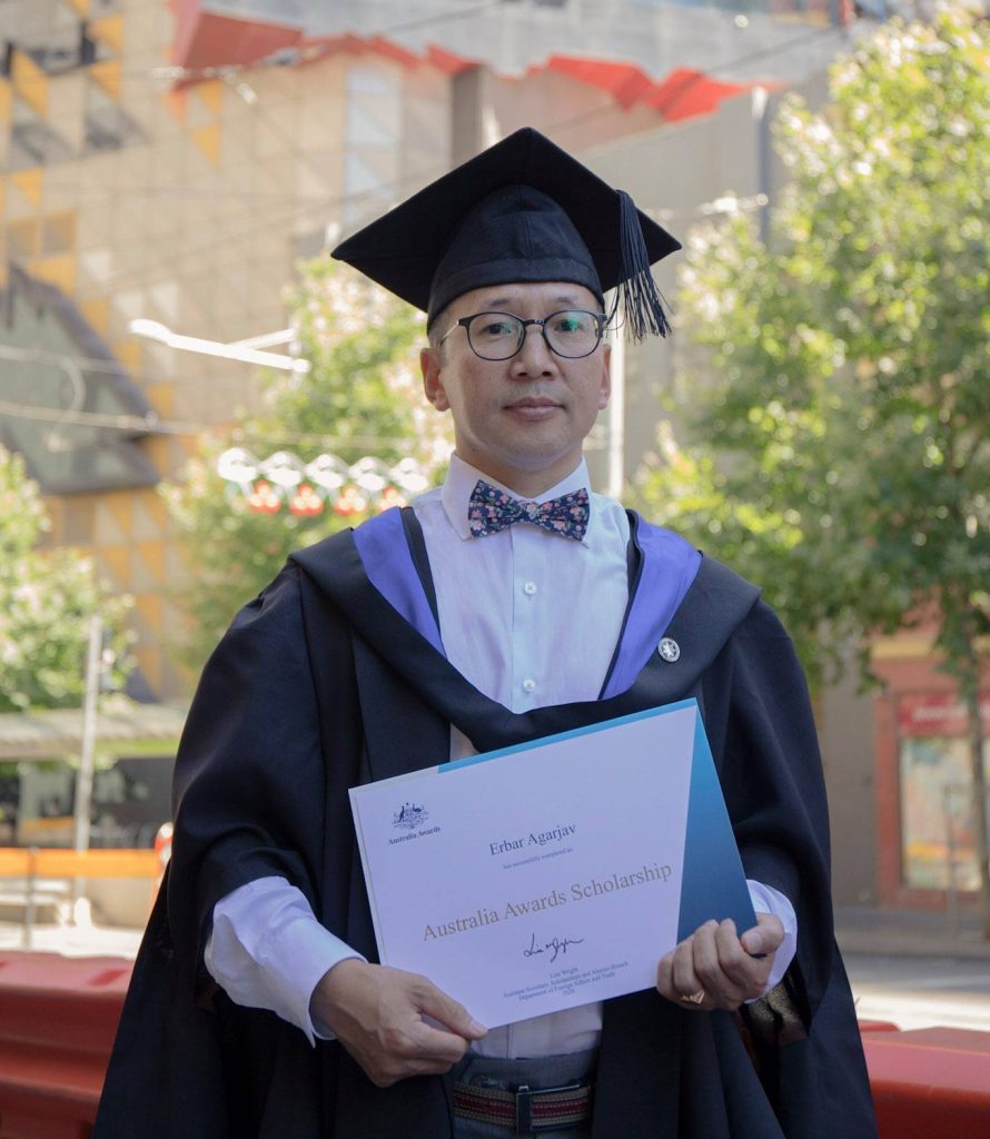 Image of Erbar holding his Australia Awards Scholarship certificate on graduation day at RMIT University.