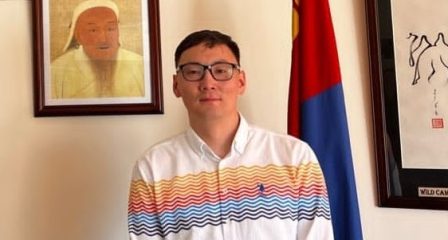 Mongolian Australia Awards alumnus standing beside the Mongolian flag