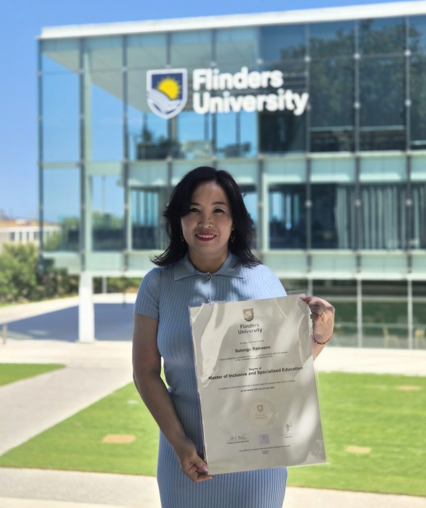 Solongo proudly holding her master's degree certificate in front of her university.